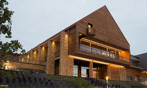 Gebäude mit Steinsäulen, Holzfassade, beleuchtetem Eingang und Balkon.