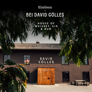 Dunkles Gebäude mit weißem Schriftzug DAVID GÖLLES, Holztür und gedecktem Tisch davor.